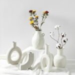 A white minimalist sculptural ceramic vase with an open-center design, styled with dried flowers