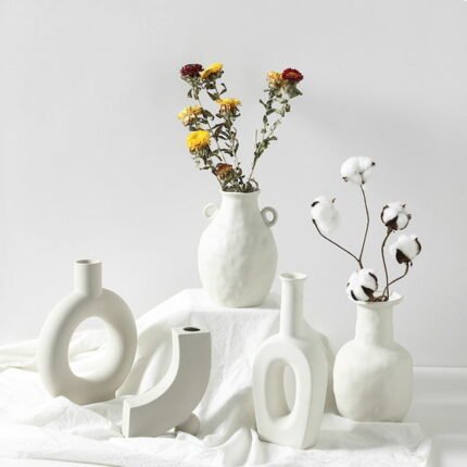 A white minimalist sculptural ceramic vase with an open-center design, styled with dried flowers