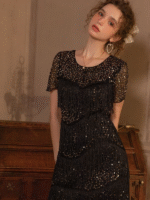 Woman wearing a vintage-inspired fringe and sequin midi dress in black-gold, standing in an elegant setting.