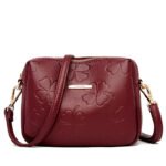 "Embossed clover crossbody bag in burgundy with adjustable strap." "Elegant emerald green embossed clover crossbody bag."