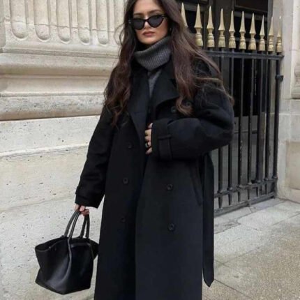 Woman wearing an oversized wool coat with leather shorts and ankle boots, showcasing chic layering style.