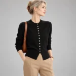 Black crew-neck button-down cardigan with long sleeves and ribbed hem, styled with beige trousers.
