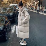 Model wearing a beige oversized puffer coat, styled with sneakers and jeans for a casual winter look. Two models wearing brown and blue puffer coats against a mountain backdrop.