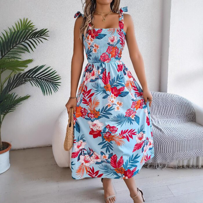 Model wearing a tropical floral smocked midi dress in yellow, teal, and sky blue, paired with a woven handbag.