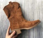 Close-up of tan suede Western boots on white fur with denim jeans Woman wearing tan cowboy boots on stairs styled with cozy sweater and black leggings