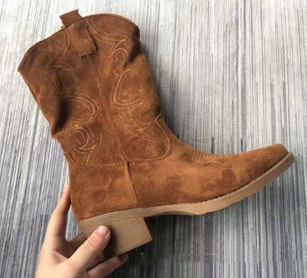 Close-up of tan suede Western boots on white fur with denim jeans Woman wearing tan cowboy boots on stairs styled with cozy sweater and black leggings