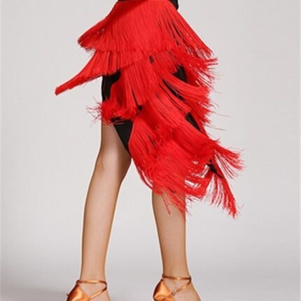 Dancer wearing red Latin dance fringe skirt with fishnet tights and gold heels on white background