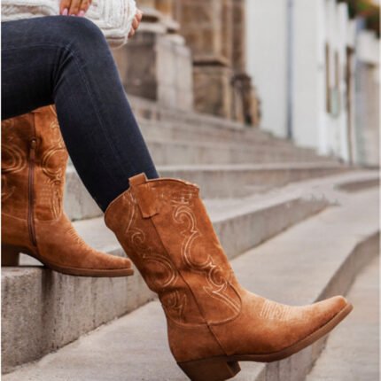 Close-up of tan suede Western boots on white fur with denim jeans Woman wearing tan cowboy boots on stairs styled with cozy sweater and black leggings