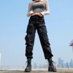 Woman wearing black multi-pocket cargo pants with boots, standing on rooftop in cityscape background.