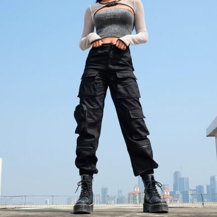 Woman wearing black multi-pocket cargo pants with boots, standing on rooftop in cityscape background.