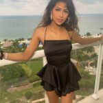 Woman wearing a black halter peplum mini romper on a balcony with an ocean view