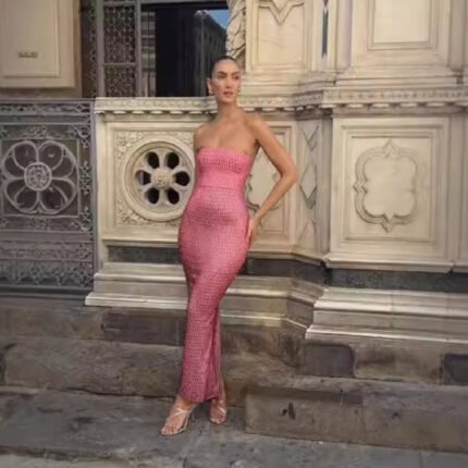Woman wearing sequin mesh backless gown at sea during sunset Woman in metallic pink mesh gown posing near elegant architecture