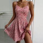 Woman wearing a blush pink spaghetti strap mini dress with white floral print.