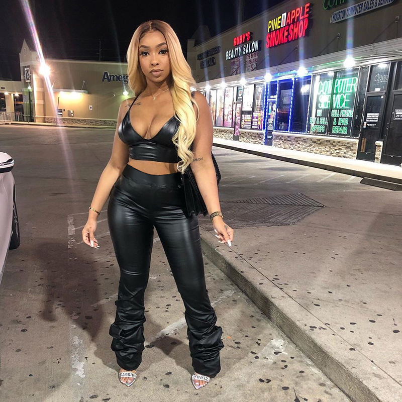 Woman wearing high waist black faux leather pants with ruched stacked leg detail, styled with crop top and heels for night out streetwear look.