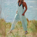 Relaxed fit sleeveless jumpsuit with pockets in neutral tones, styled with sneakers for casual wear.