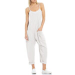 Relaxed fit sleeveless jumpsuit with pockets in neutral tones, styled with sneakers for casual wear.