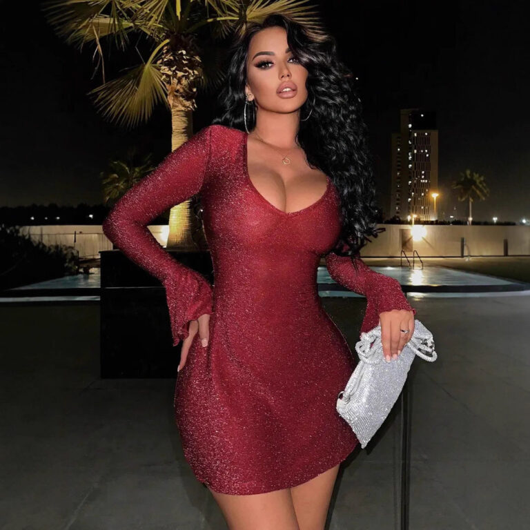 Model wearing a red glitter mini dress with a deep scoop neckline, fitted silhouette, long sleeves, and flared bell cuffs.